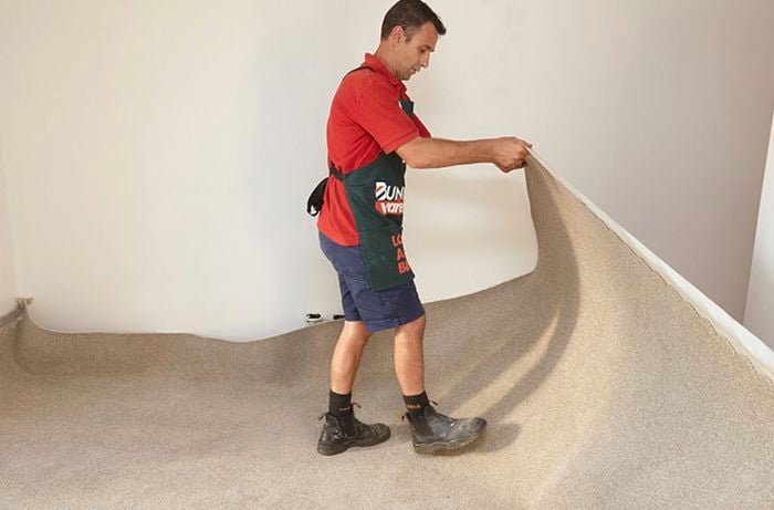A Bunnings team member rolling out carpet into a cream-coloured room
