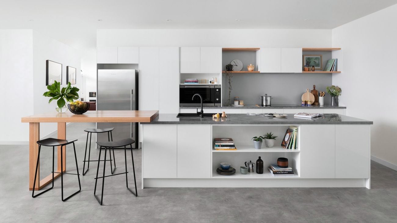 A spacious modern kitchen with white cupboards, steel appliances, shelving, an extended wooden island with bar stools, and other decor.