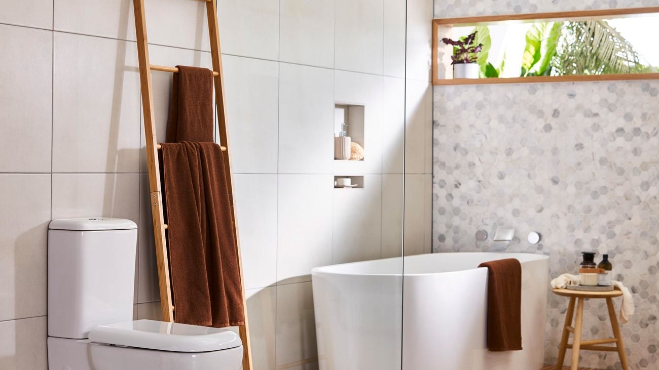 Bathroom featuring large-tiled walls, bath, toilet and window with green plants outside.