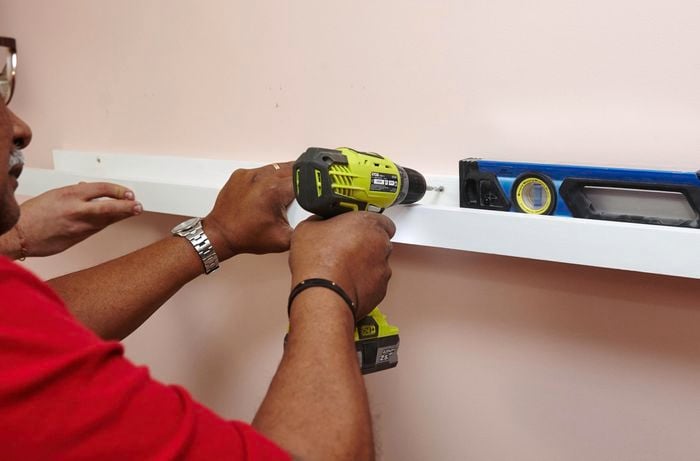 A person attaching a timber ledge to a wall using a cordless drill