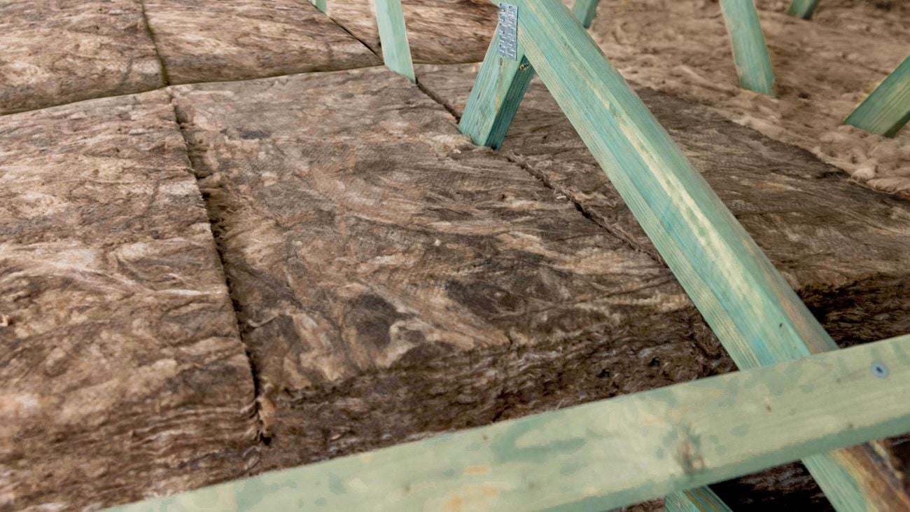Fibrous insulation batts laid between light green timber roof trusses or floor joists.