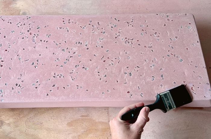 A person applies sealer to a pink terrazzo tabletop.