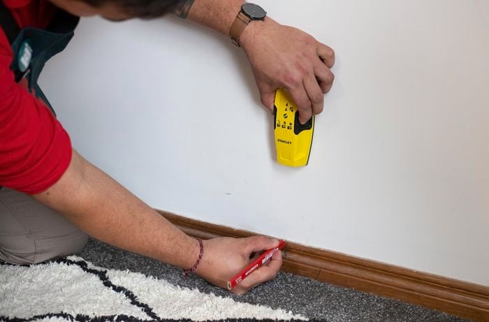 Person using stud finder against a wall and marking a spot with pencil.