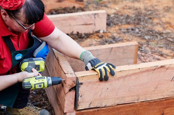 A timber sleeper being drilled into the frame for a sleeper compost bin with a power drill