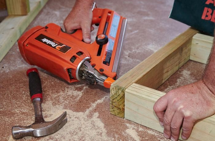 A person using a nail gun to join lengths of timber to make a frame