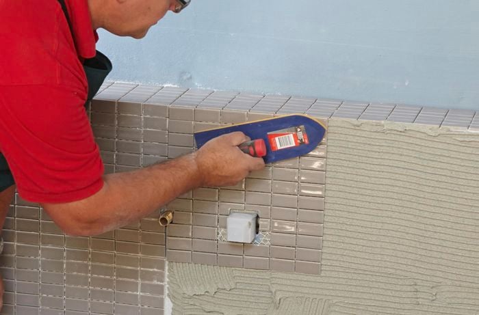 Mosaic tiles being applied to a vertical feature wall with a trowel and pre-applied tile adhesive