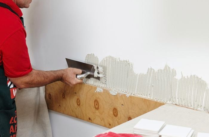 Person applying tile mastic to wall.