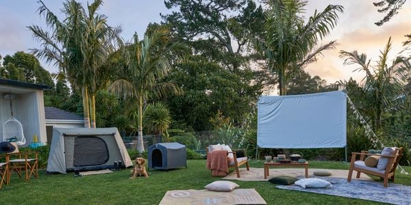 Outdoor set up of towels and cinema with fairylights and white sheet to make up outdoor cinema. 