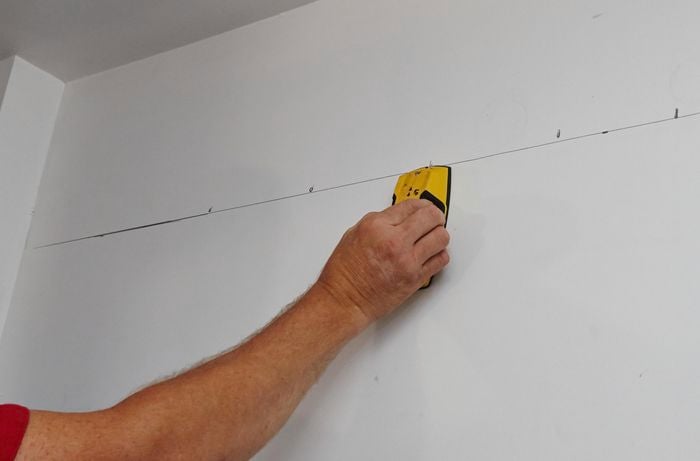 A stud finder being used to locate studs in the wall at the back of a walk in wardrobe