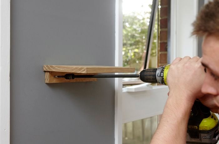 A person screwing a shelf to a wall using a cordless drill and extension drill bit