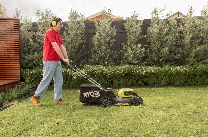A Bunnings Team Member wearing ear protection is mowing a lawn before aerating with a Ryobi lawnmower