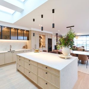Modern open-plan kitchen and dining area featuring a large island bench, light timber cabinetry, pendant lighting and skylights.