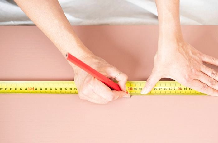 Measuring and marking shelf positions on a painted wall panel using a tape measure and pencil.