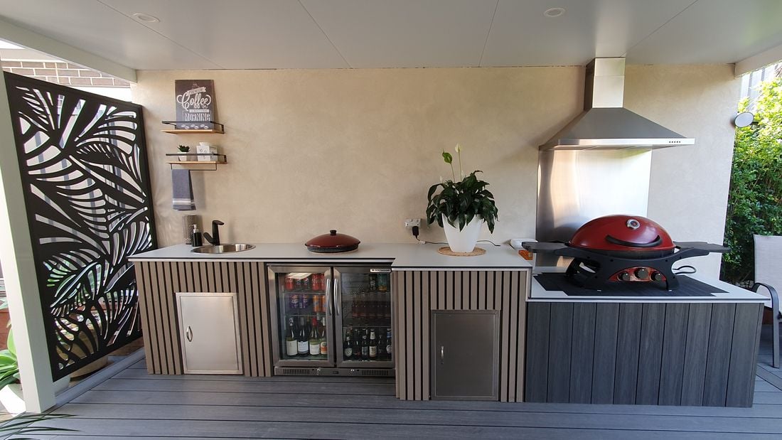 Outdoor entertaining area with bbq, fridge, rangehood all sitting on outdoor grey decking.