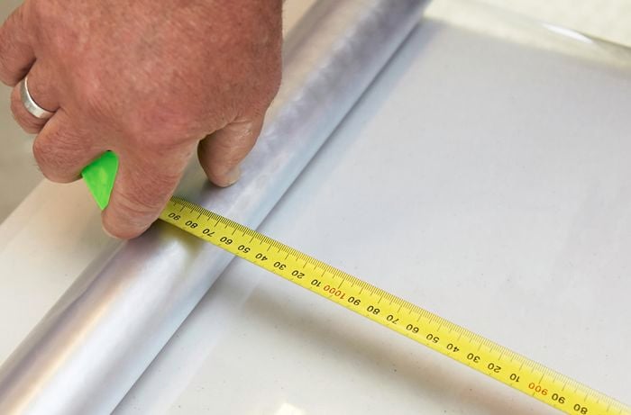 A person measuring a frosting sheet using a measuring tape
