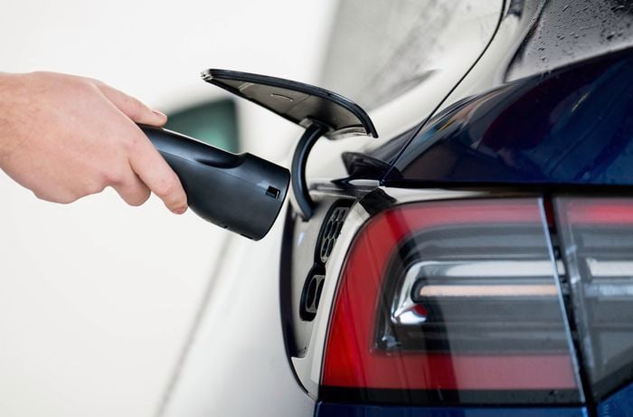 : A person is plugging a Tesla EV charging connector into the charging port of an electric car.  ]