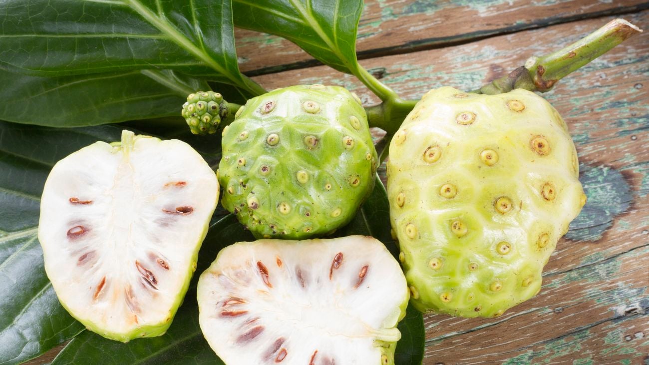 Noni fruit, some cut in half, on an outdoor table