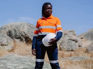A lady wearing work site clothing and holding a white helmet.