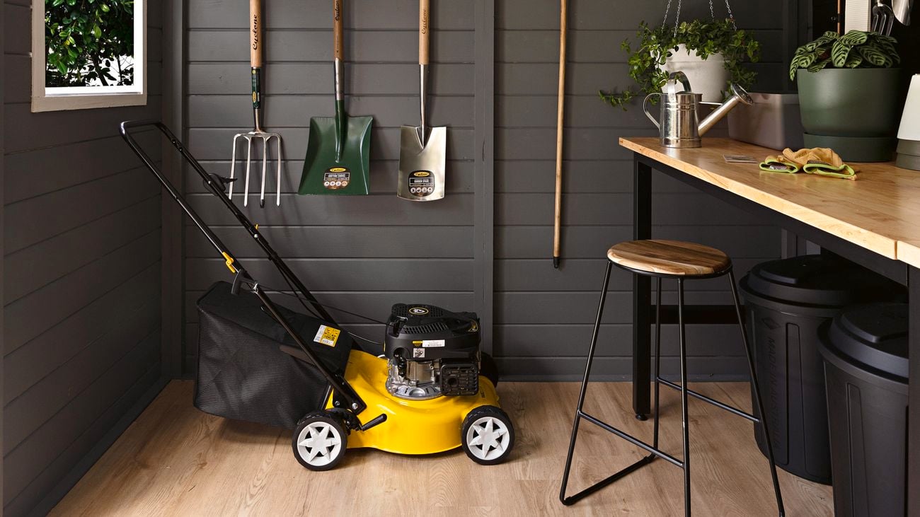 Interior of a charcoal potting shed featuring hanging storage, lawn mower and a workbench