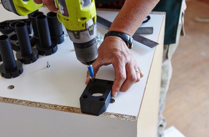A person positioning the base for an adjustable foot on the underneath of a cabinet