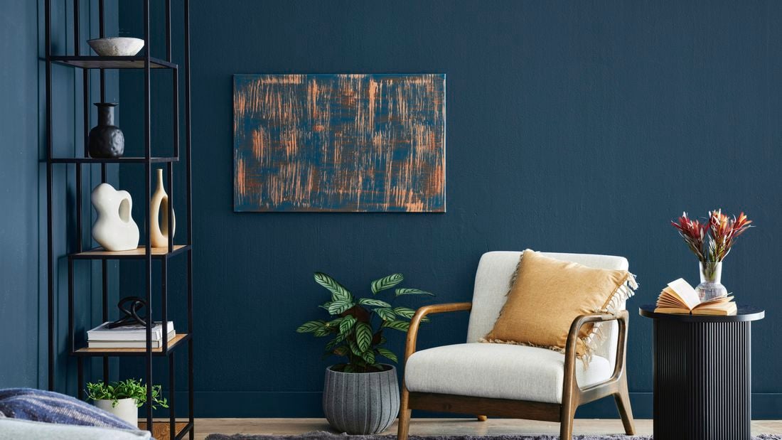 A bold blue and orange canvas print mounted on the wall, cream chair, grey rug and indoor plant