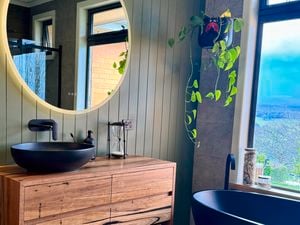 Renovated bathroom with black round basin, black tapeware, round mirror hanging on wall.
