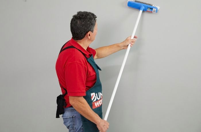 A man prepares a wall for paint with a soft-bristled broom.