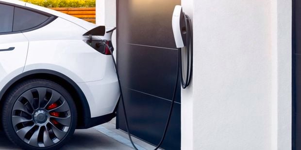 Close up of a Tesla car being charged with a Tesla EV charger at the front of a house