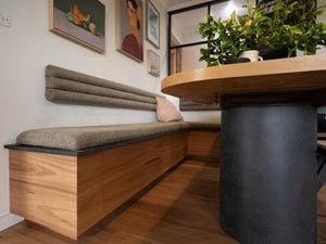 Fully completed storage bench seat attached to a wall and a round table next to it.
