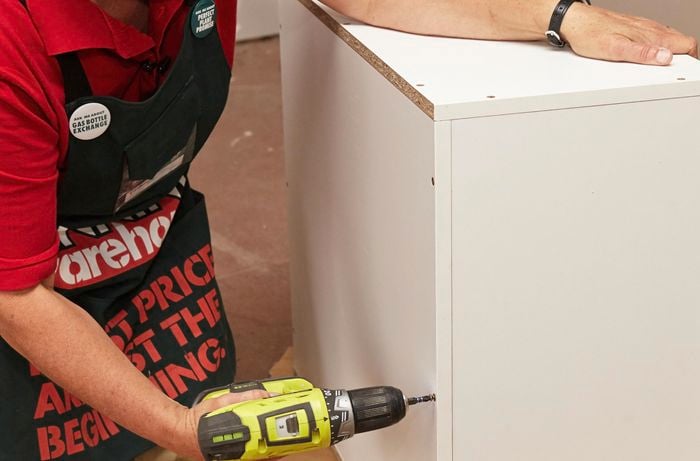 Person attaching  base and top panels of cabinet using a drill