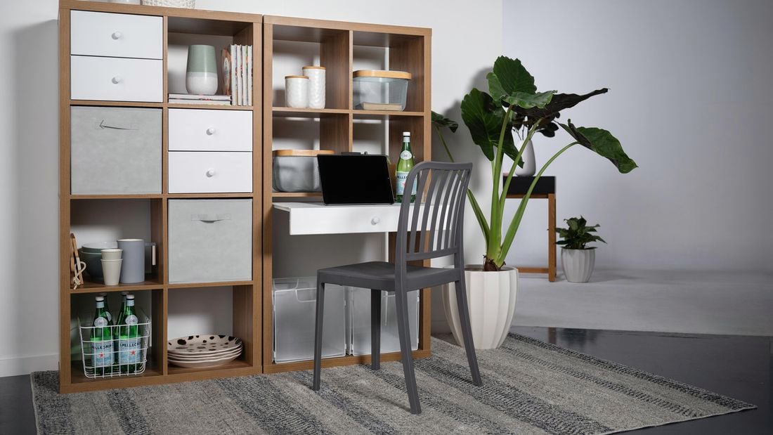 A shelving unit next to a wall with shelves and drawers in it, a plant next to it and a chair in front of it