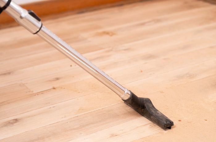 A vacuum is used to clean sanding dust from the floor surface before continuing with finer grit sanding.