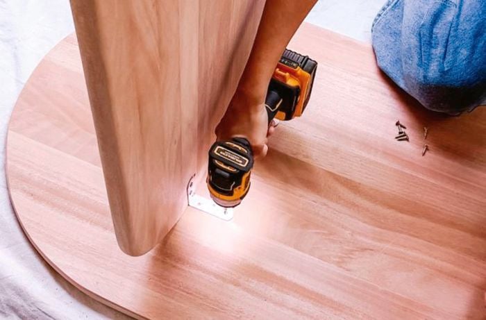 Person using drill to attach brackets to the underneath of the table top and inside of the table leg.