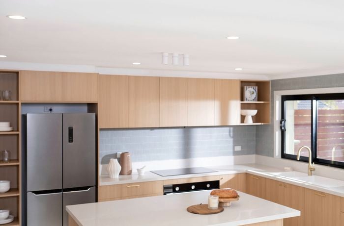 : A modern kitchen with light wood cabinets, a large island, and a window over the sink that lets in natural light, complemented by kitchen-suitable lighting fixtures. 