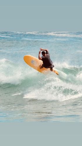 Surfer hitting the top of a wave on a yellow Summer vibes softboard with spray flying.