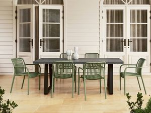 Outdoor dining table with olive green slatted chairs, on a paved patio in front of white French doors