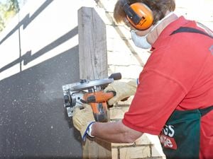 Person wearing ear protection cutting a fence post using a circular saw