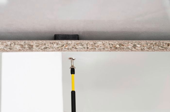  A person is using a power drill to drill through the back panel into the wall to fix the cabinet. ] 