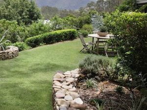 Backyard with green lawn, rocks, outdoor furniture and trees.
