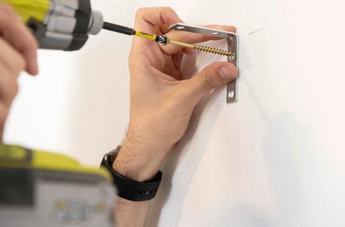 Brackets for a wall mounted cube shelf being screwed into the wall with a power drill