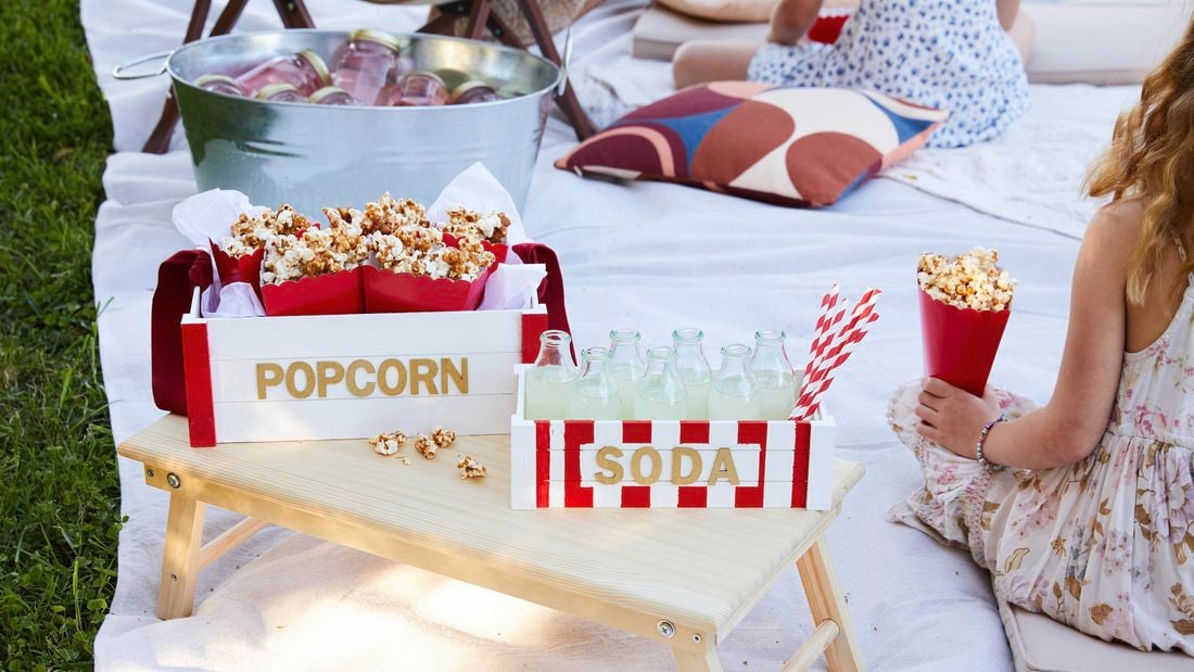 Soda and popcorn tray sitting on a bed tray while in a picnic style movie night is happening