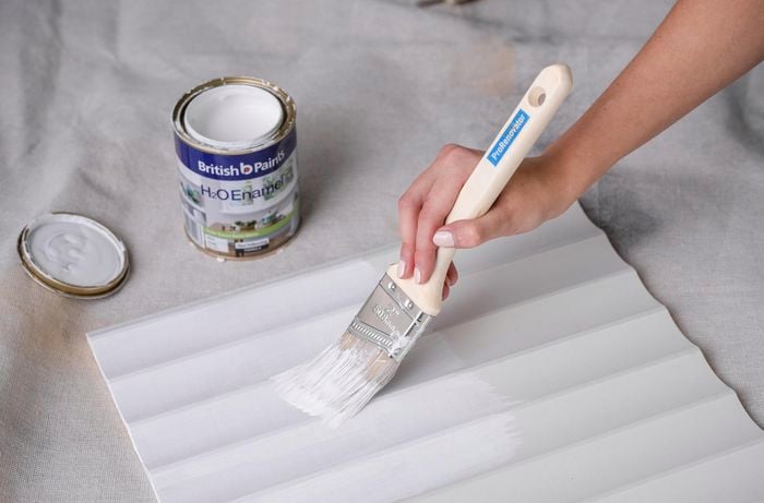 A scallop panel being painted white with a paintbrush
