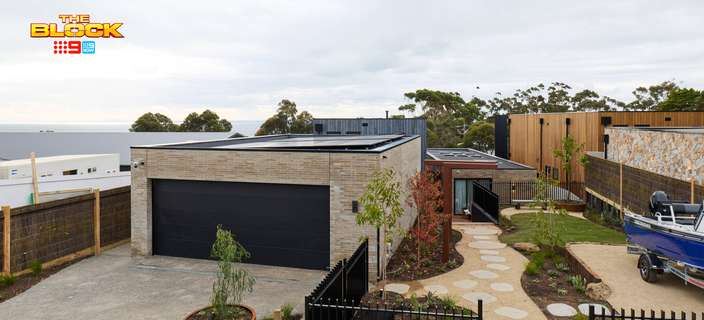 Modern home exterior featuring a double garage, landscaped garden, stone stepping path, black metal fencing and a parked boat.