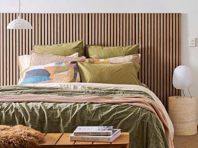A bedroom showing a bed with a timber headboard, cosy blankets and pillows to help with home insulation