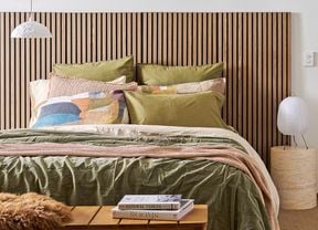 A bedroom showing a bed with a timber headboard, cosy blankets and pillows to help with home insulation
