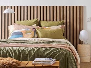 A bedroom showing a bed with a timber headboard, cosy blankets and pillows to help with home insulation