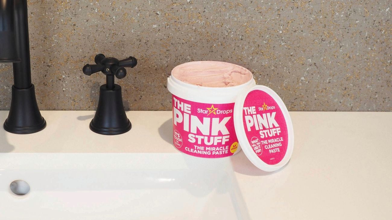 A tub of The Pink Stuff cleaning paste on a bathroom vanity beside a black tap.