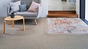 Living room with white brick wall, grey couch, timber coffee table and carpeted floors.