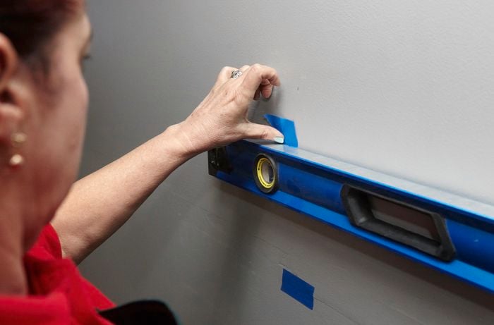 A person using a spirit level to place masking tape on a wall