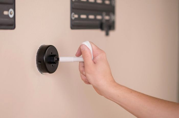 A hand twisting a hole saw to drill into the wall.